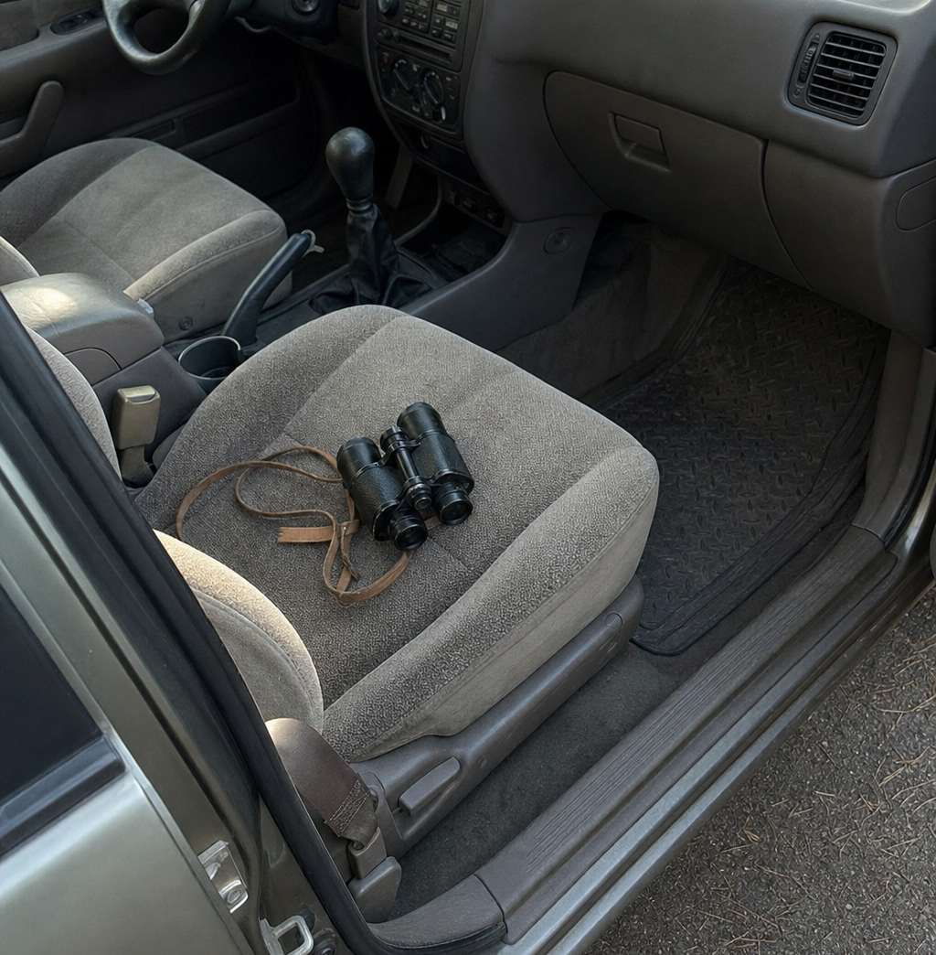A worn pair of binoculars on a car seat, seen from the open passenger door