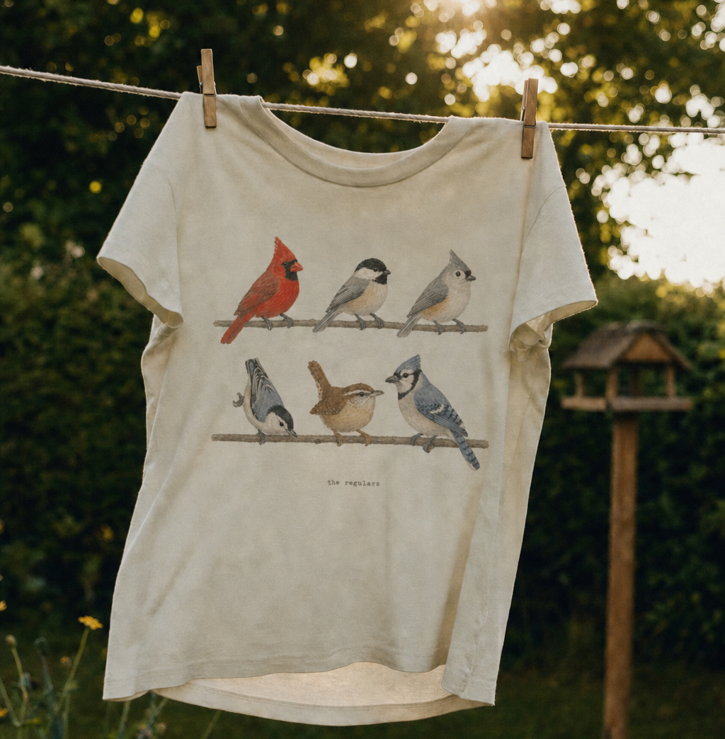 A Spark Bird Society tee on a clothesline in a backyard, a bird feeder behind it