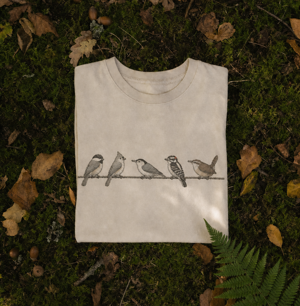 A Spark Bird Society tee laid on moss and autumn leaves
